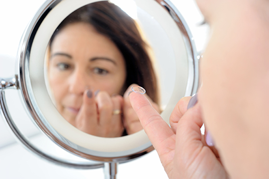 Middle Aged Woman Looking Into Makeup Mirror to Insert Contact Lens Into Eye